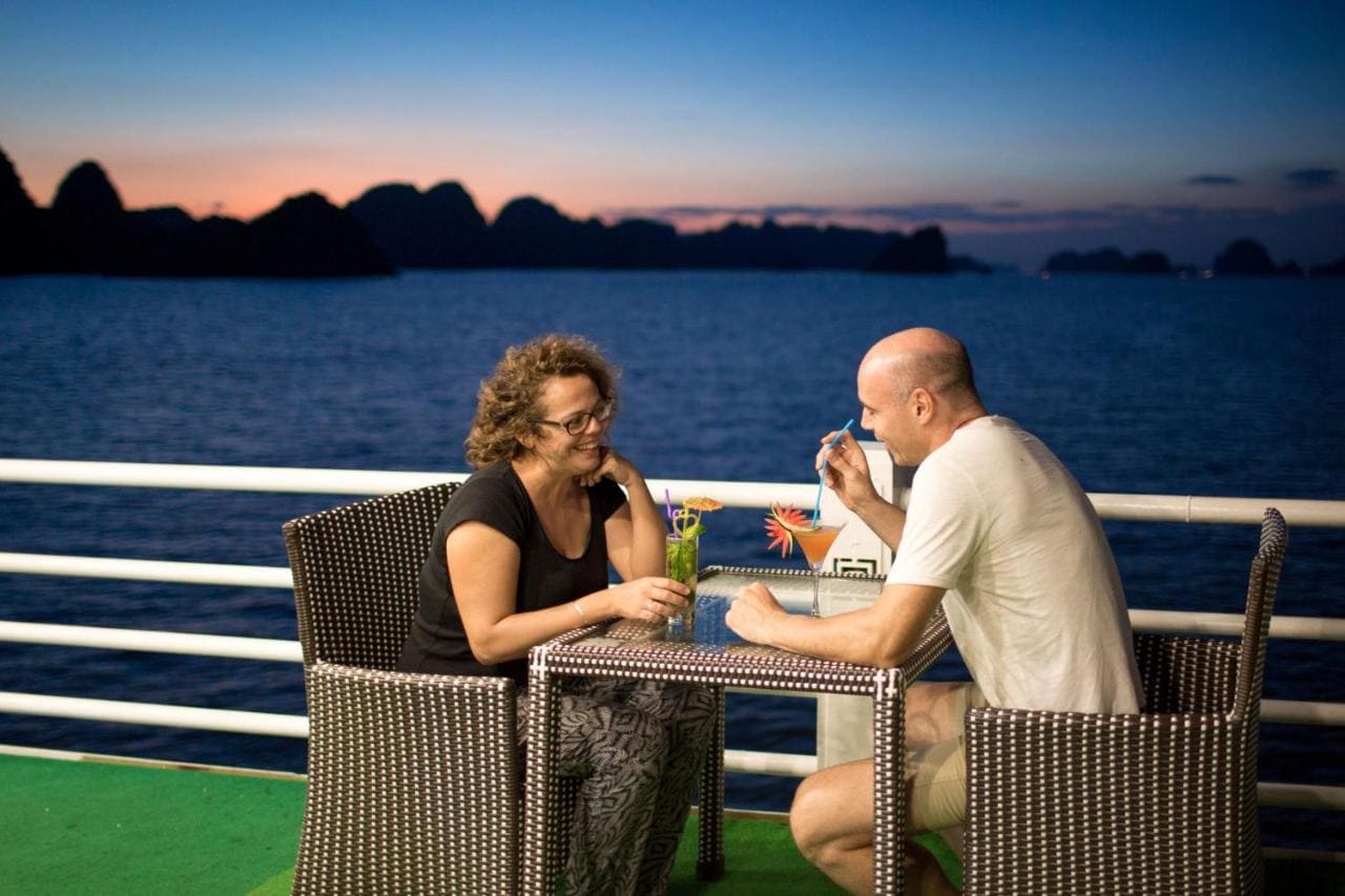 7 Best HaLong Bay Cruises for an Epic Journey 23 Couple with cocktails on La Regina Royal cruise deck at sunset, romantic HaLong Bay cruises.