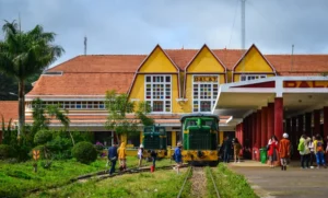 The Da Lat Railway Station’s yellow facade under morning light, with its three peaked roofs and a vintage train parked on the tracks.